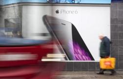 A bus and pedestrian pass an advertisement for the Apple iPhone 6 in north London